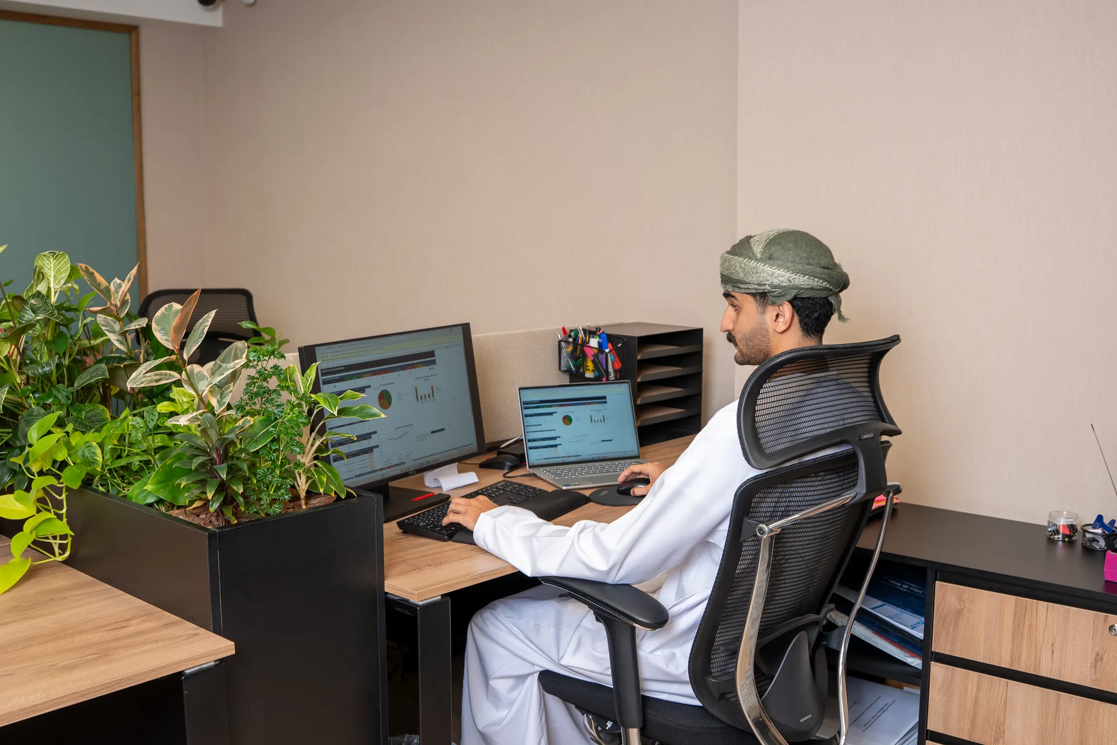 Omani professional reviewing investment dashboards at his desk